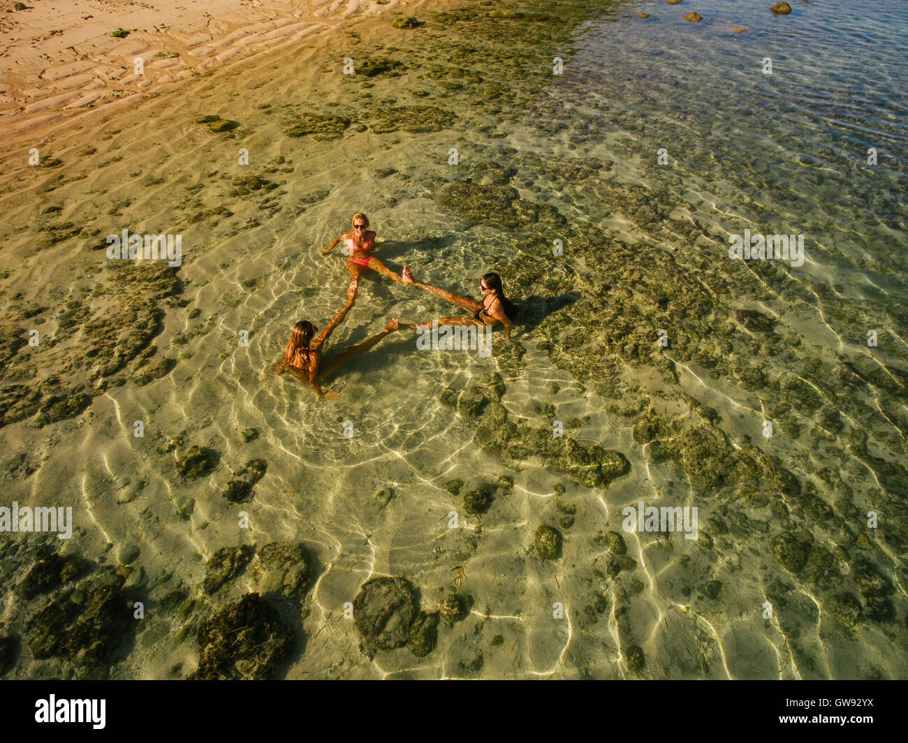 Luftaufnahme von drei jungen Frauen sitzen im Meerwasser mit den Füßen berühren und eine Ausbildung zu machen. Freundinnen entspannen ich Stockfoto