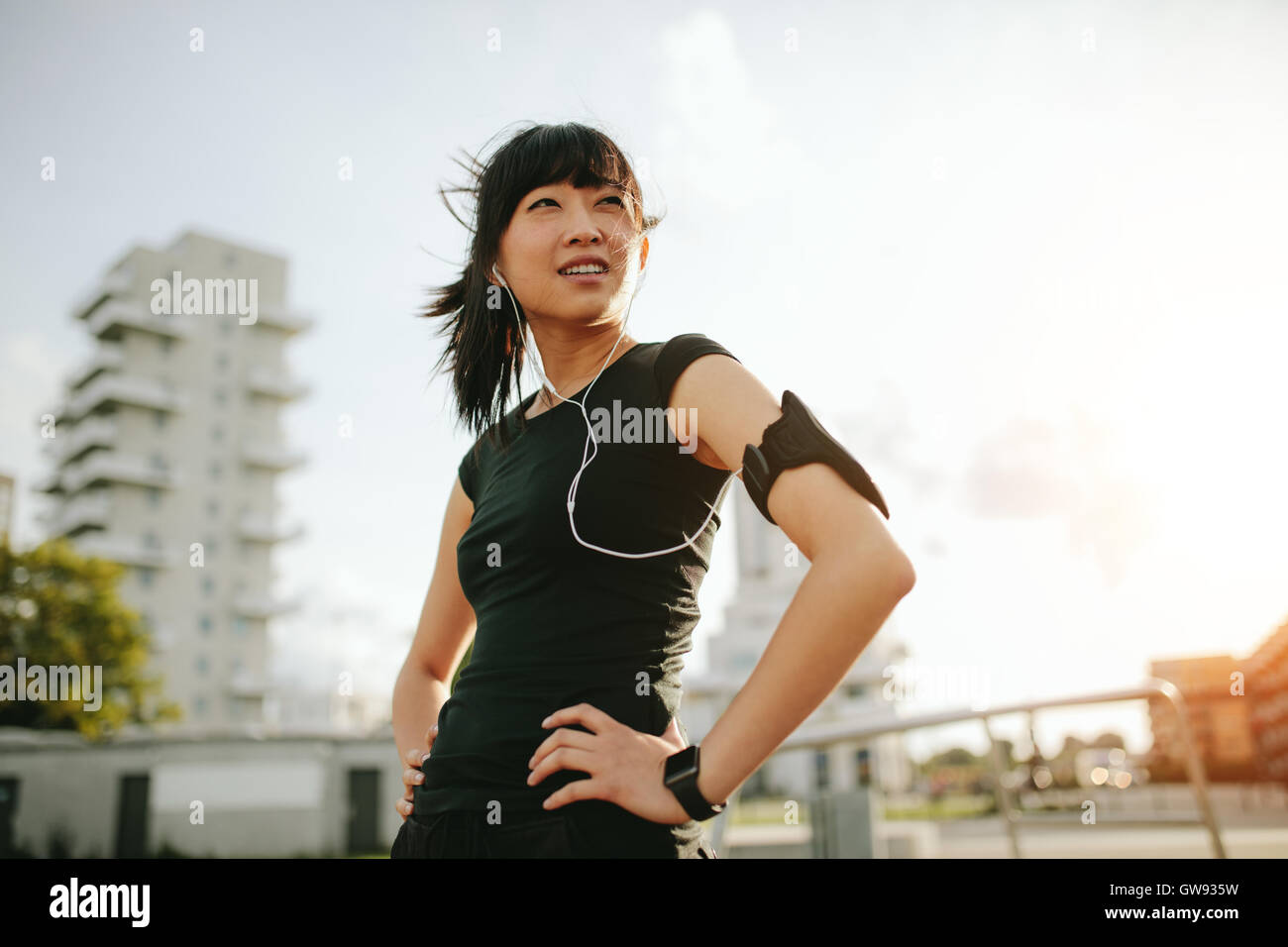 Schuss einer jungen asiatischen Frau, die während des Morgenlaufs eine Pause macht. Fitness-Frau steht draußen mit Händen auf den Hüften und sieht aw aus Stockfoto