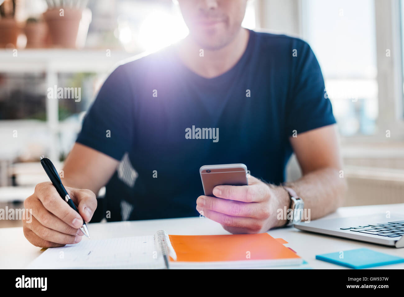 Geschäftsmann mit Handy während des Schreibens im Tagebuch. Schuss von Mannhände an seinem Schreibtisch arbeiten hautnah. Stockfoto