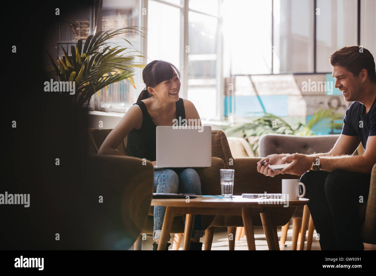 Aufnahme von zwei Geschäftspartner sitzen im Büro Lobby und lächelnd. Frau mit Laptop diskutieren Geschäftsideen mit männlichen colleag Stockfoto