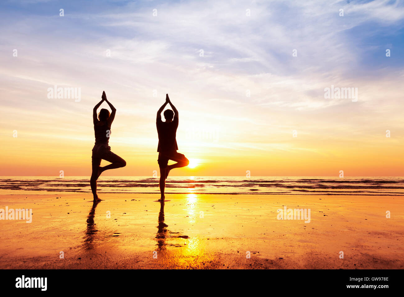 Zwei Menschen praktizieren Yoga Baum Lage am Strand mit wunderschönen Sonnenuntergang und Reflexion Stockfoto