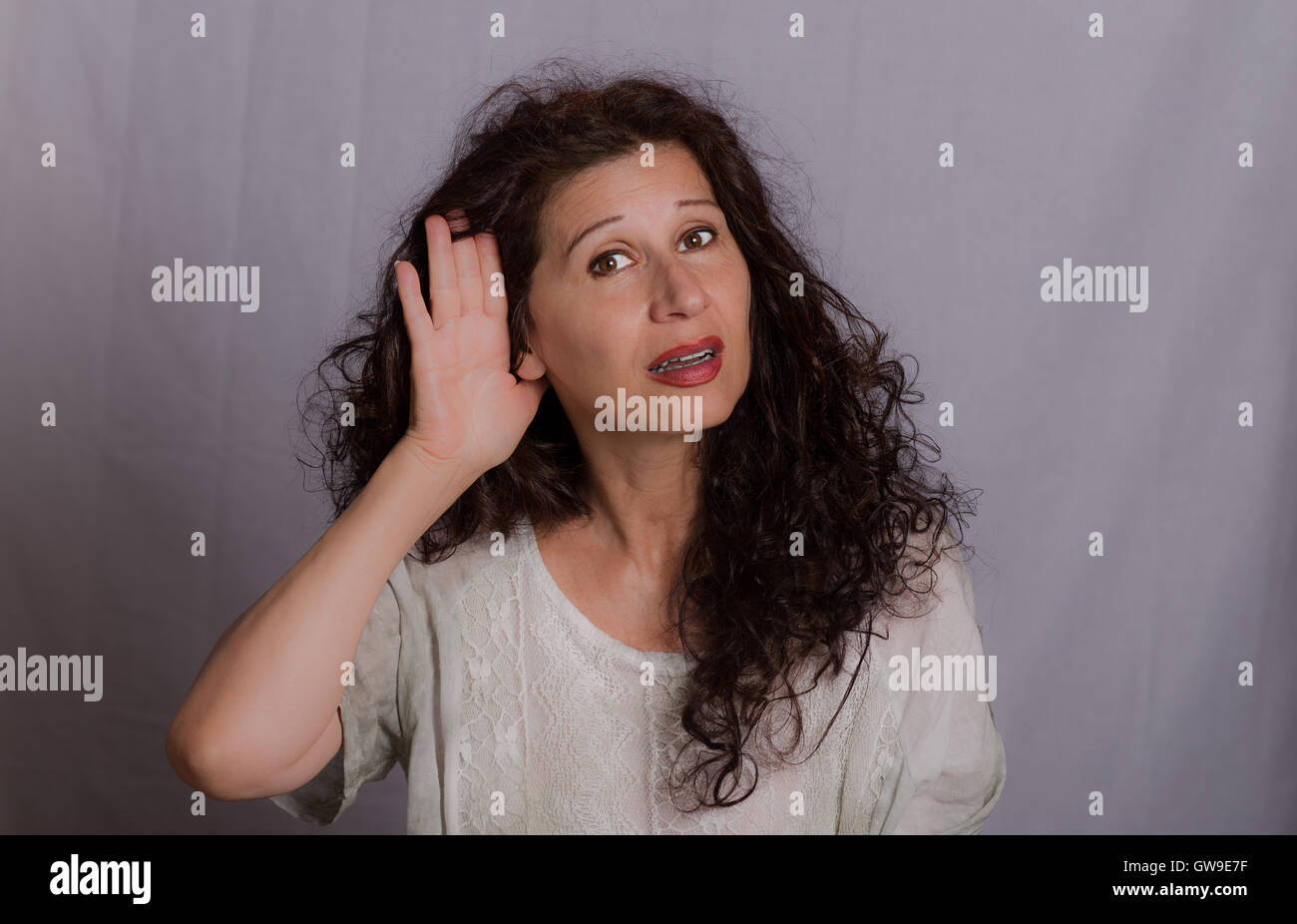 Reife Frau Platzierung Hand auf hören wegen Hörproblemen oder Beeinträchtigung auf grauem Hintergrund Stockfoto