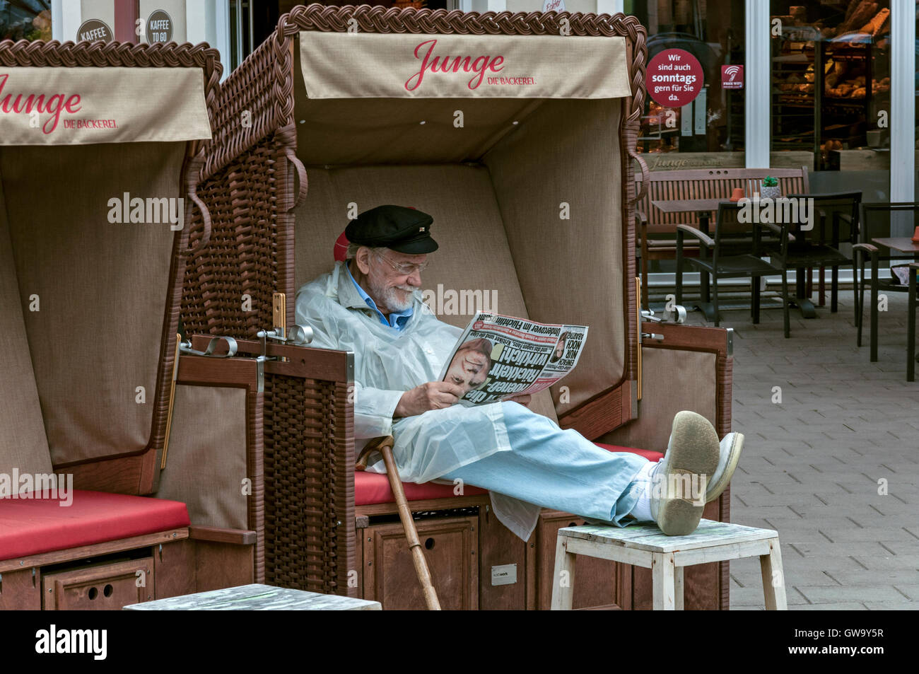 Senioren, die Zeitung zu lesen, während im Strandkorb in einem Café an der Ostseeküste in Deutschland sitzen Stockfoto