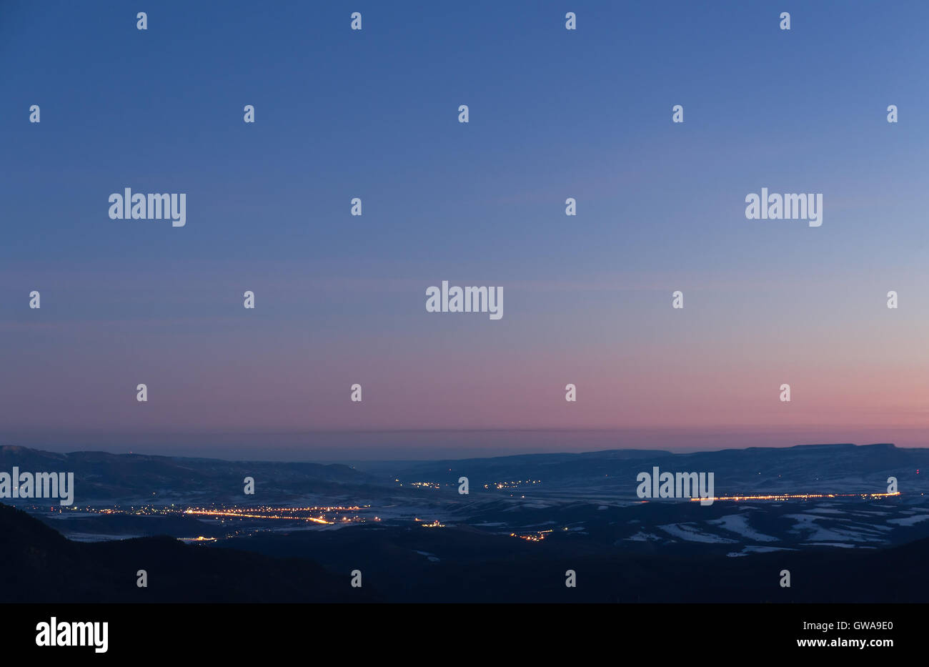 Zeigen Sie Winter am frühen Morgen aus den Bergen ins Tal mit den Städten ausstrahlen des Lichtes und mit blauem Himmel rosa an Stockfoto