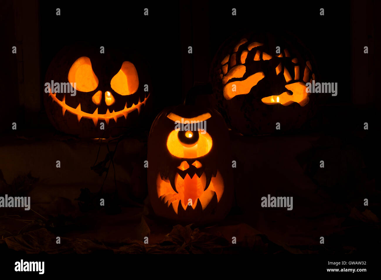 Fotomontage von drei Kürbisse für Halloween. Jack, einem Zyklopen und Hände des Kürbis gegen Herbstlaub und Kerzen Stockfoto