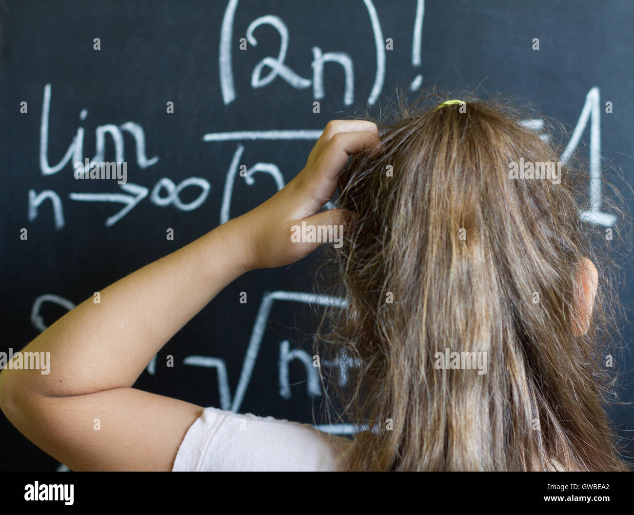 Schulmädchen denkt an die schwierige Aufgabe der Mathematik auf Tafel Stockfoto
