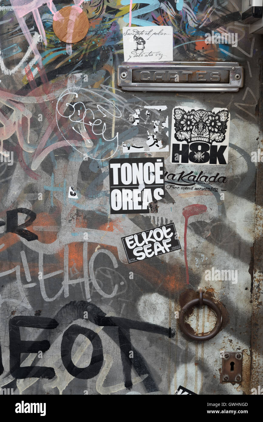Graffiti bedeckt Tür mit Briefkasten und Schlüsselloch unten einen Durchgang von Casa Bruno Quadros, Barcelona, Spanien. Stockfoto