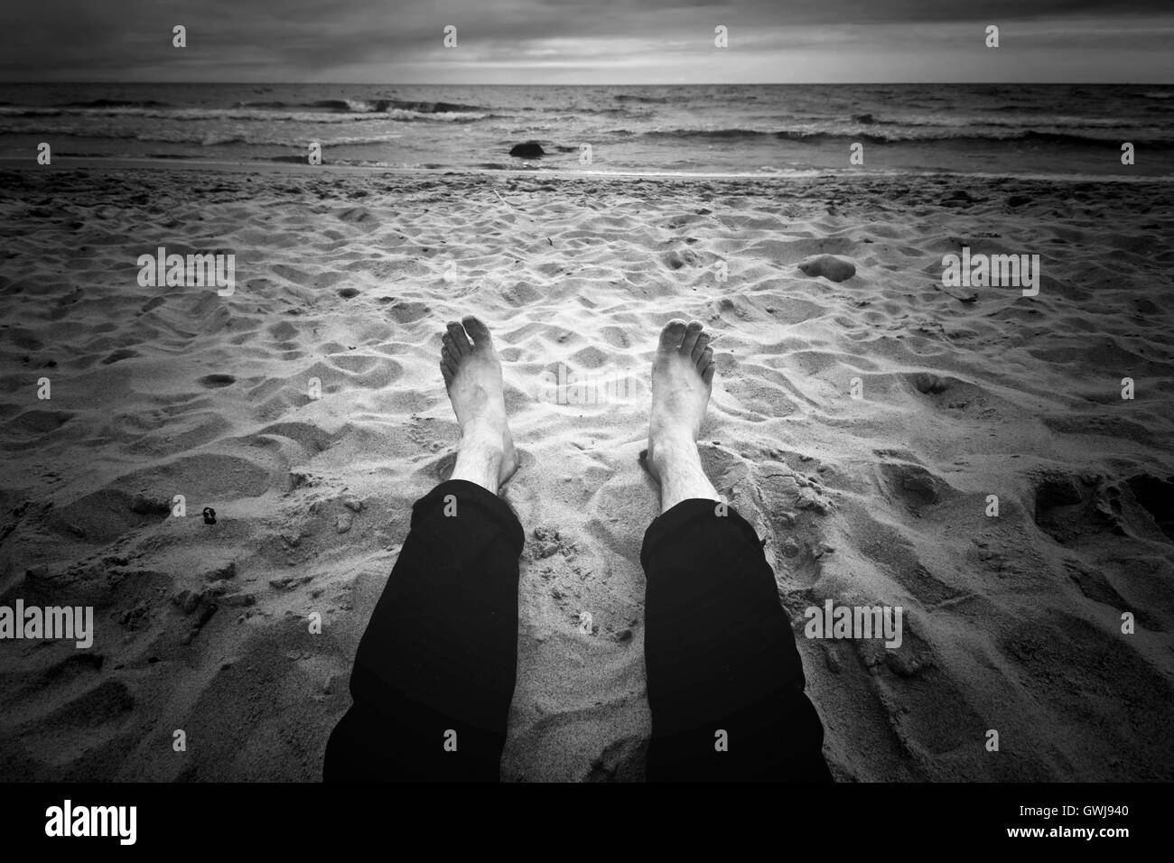 Zielort. Mann sitzt am dunklen Strand in der Nähe von Meer. Schwarz / weiß Bild. Stockfoto