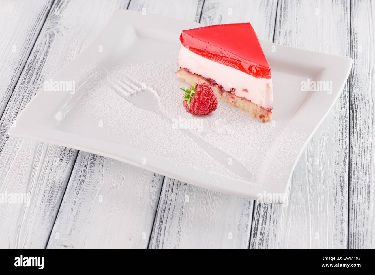 Stück Gelee-Torte mit Erdbeeren auf weißem Hintergrund aus Holz. Stockfoto