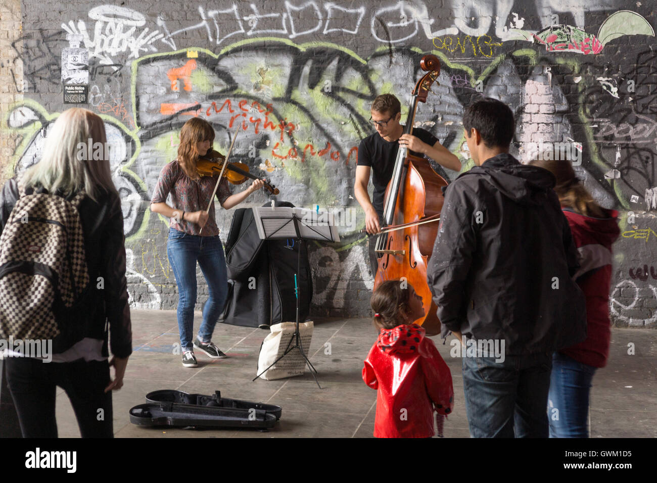 Ein paar Musiker als Straßenmusikant auf Clink Street, London, beobachtet von Passanten Stockfoto