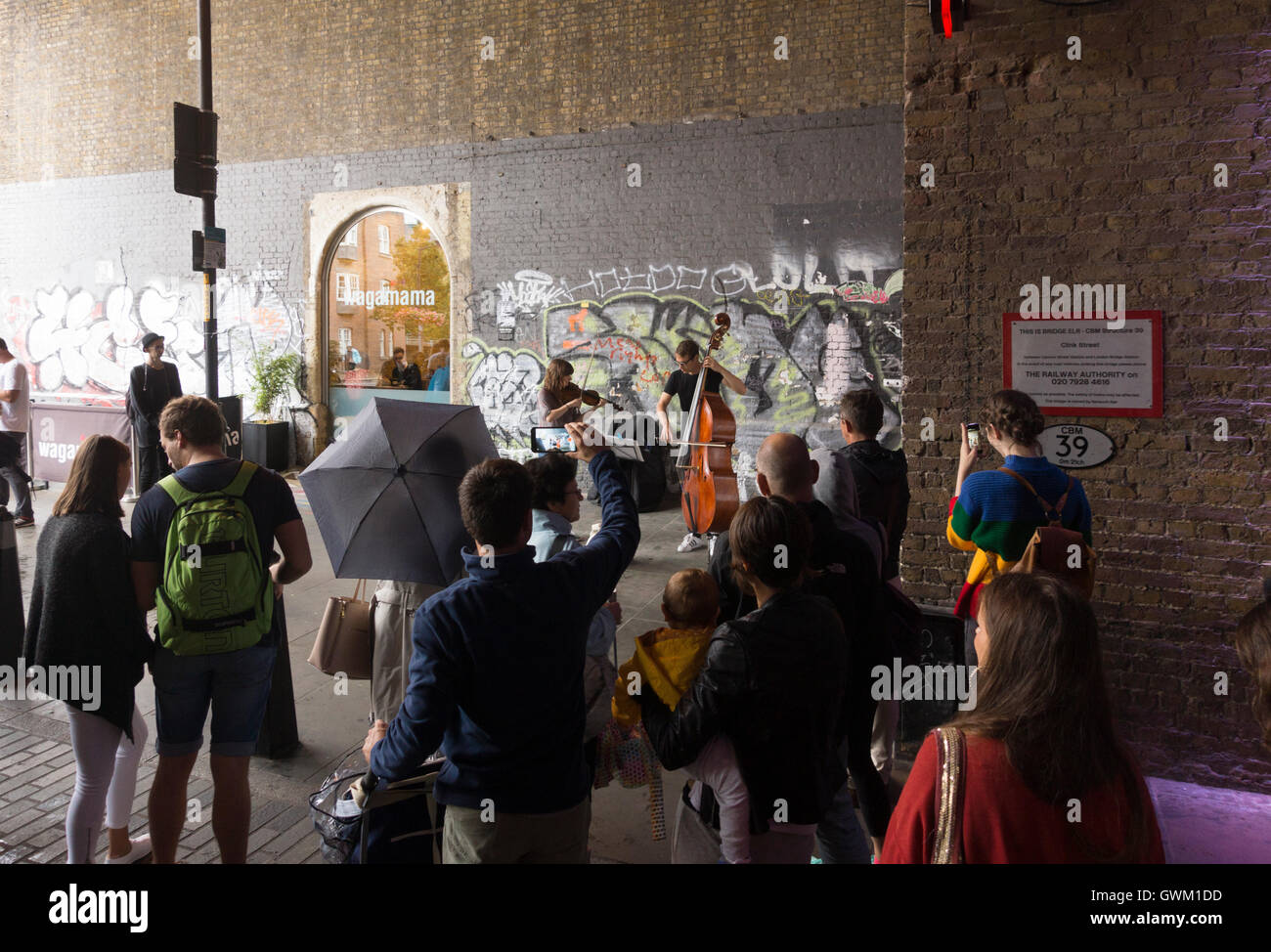 Ein paar Musiker als Straßenmusikant auf Clink Street, London, von einer Schar von Passanten beobachtet Stockfoto
