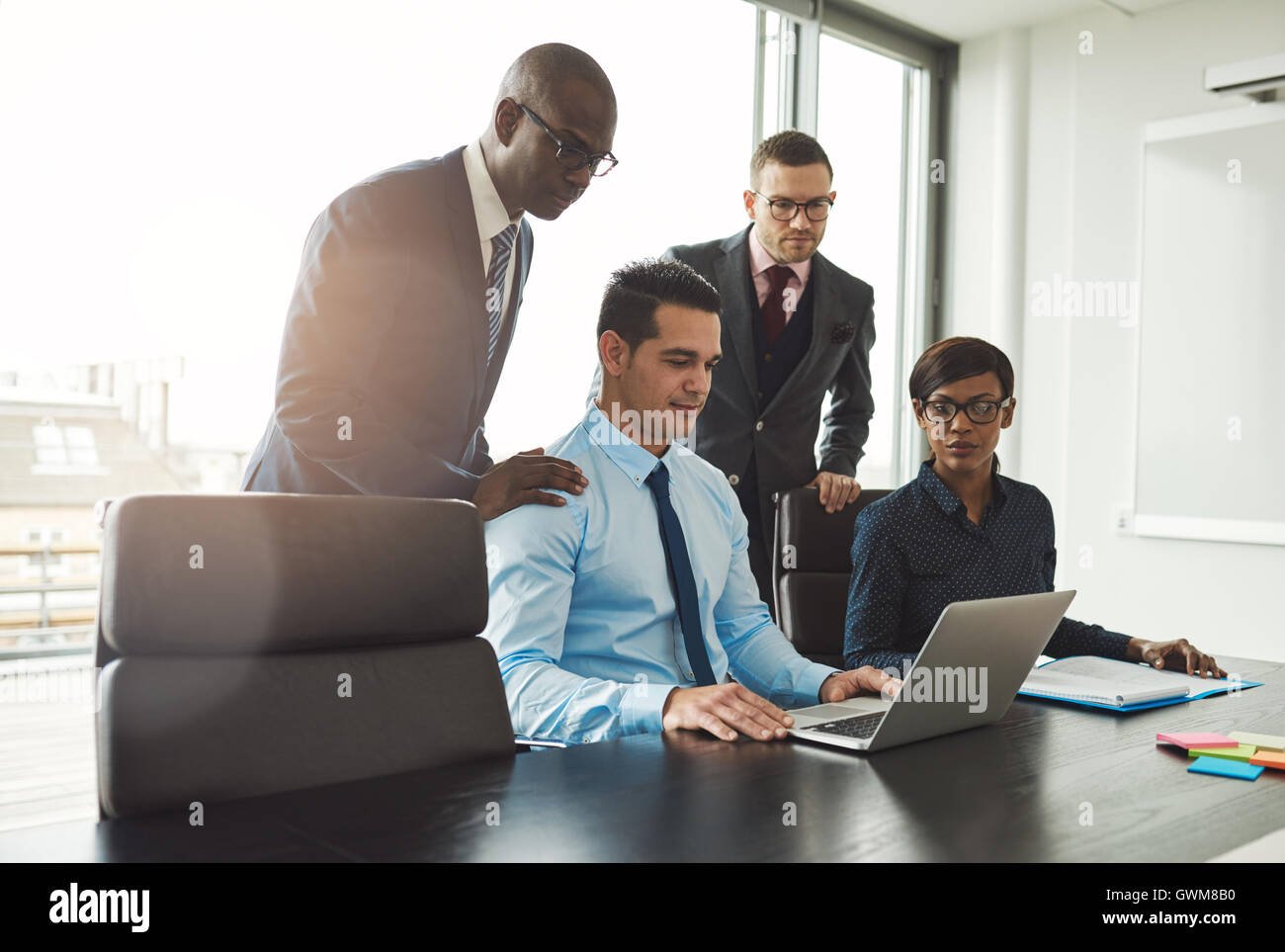 Freundliche Gruppe von vielfältigen junge Geschäftsleute in der formalen Kleidung Blick auf Laptop am Konferenztisch vor großen windo Stockfoto