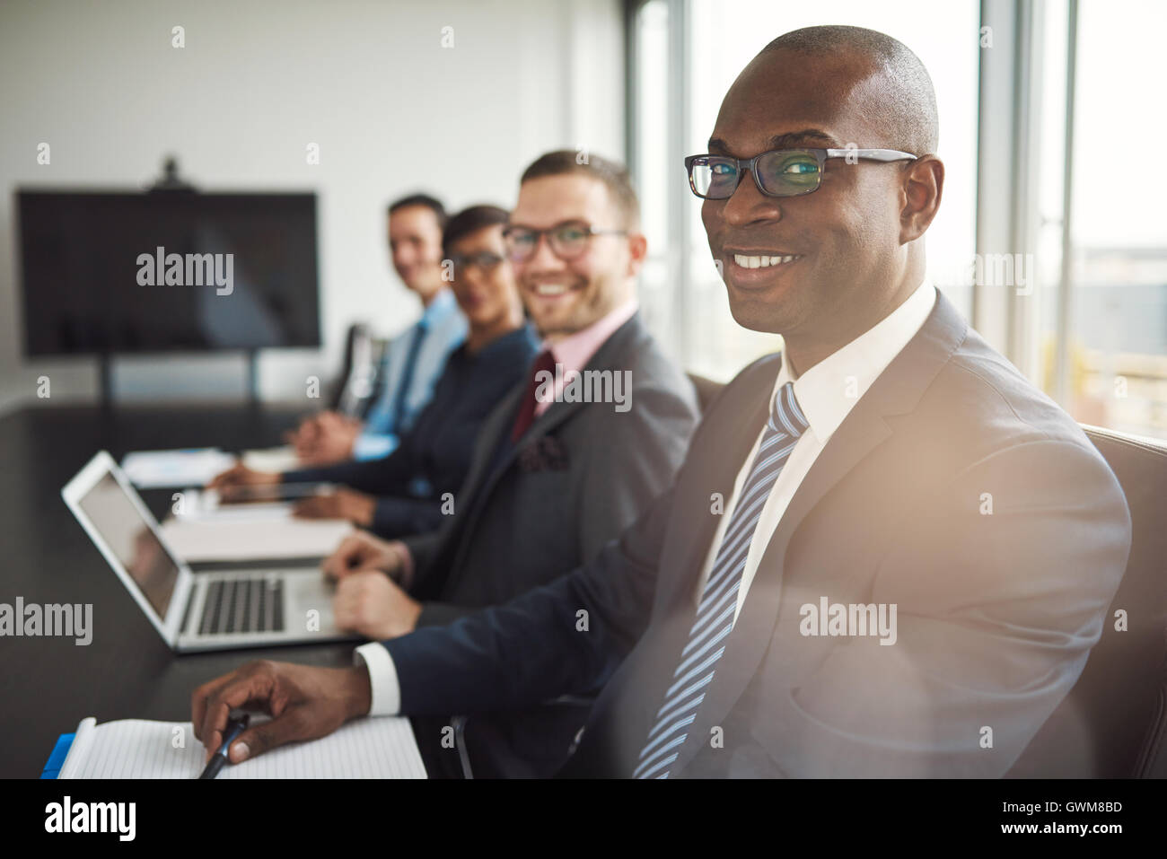 Lächelnde zuversichtlich afrikanischen Geschäftsmann in einem Gespräch mit einer Gruppe von Rassen Mitarbeiter sitzen an einem Konferenztisch in der von Stockfoto