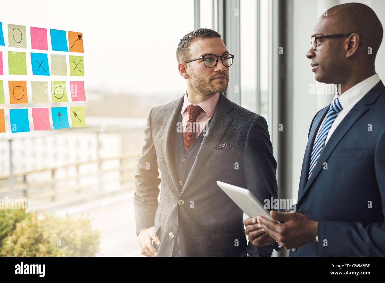 Kaukasischen und afrikanischen Geschäftsmann in einem Meeting steht vor bunten Memos auf das Glas eines Fensters in das Büro lookin Stockfoto