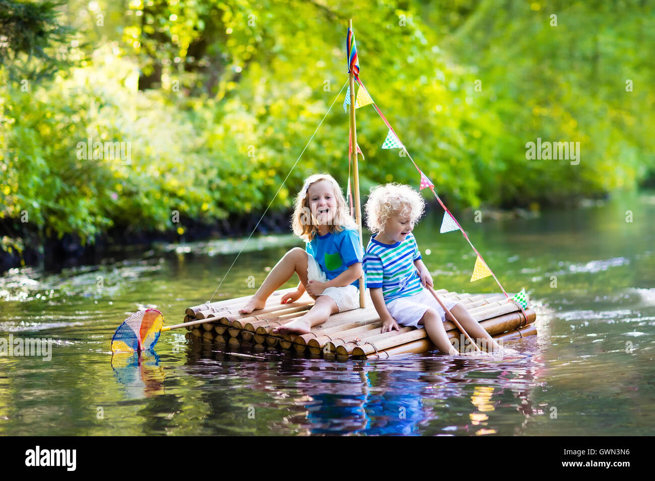 Zwei Kinder auf hölzerne Floß Fang von Fischen mit einem bunten Netz in einem Fluss und das Spiel mit Wasser am heißen Sommertag. Stockfoto