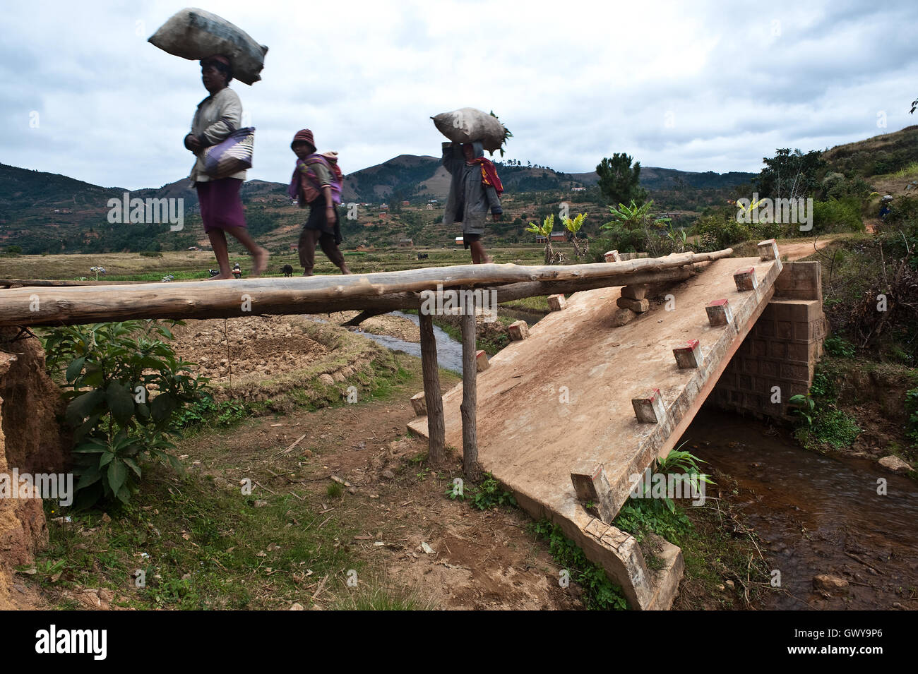 Drei Personen sind Fuß über eine kleine Holzbrücke, gemacht von einigen Stämmen ersetzte eine eingestürzte Betonbrücke (Madagaskar) Stockfoto