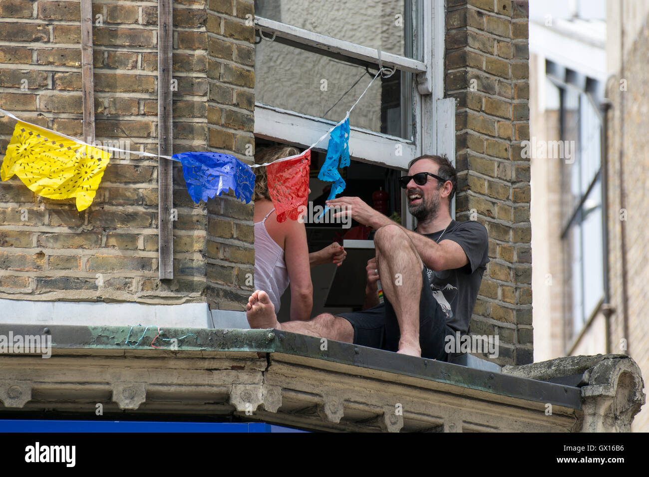 Menschen in Windows während der 50. Notting Hill Carnival feiern; Windows mit bunten Girlanden verziert Stockfoto