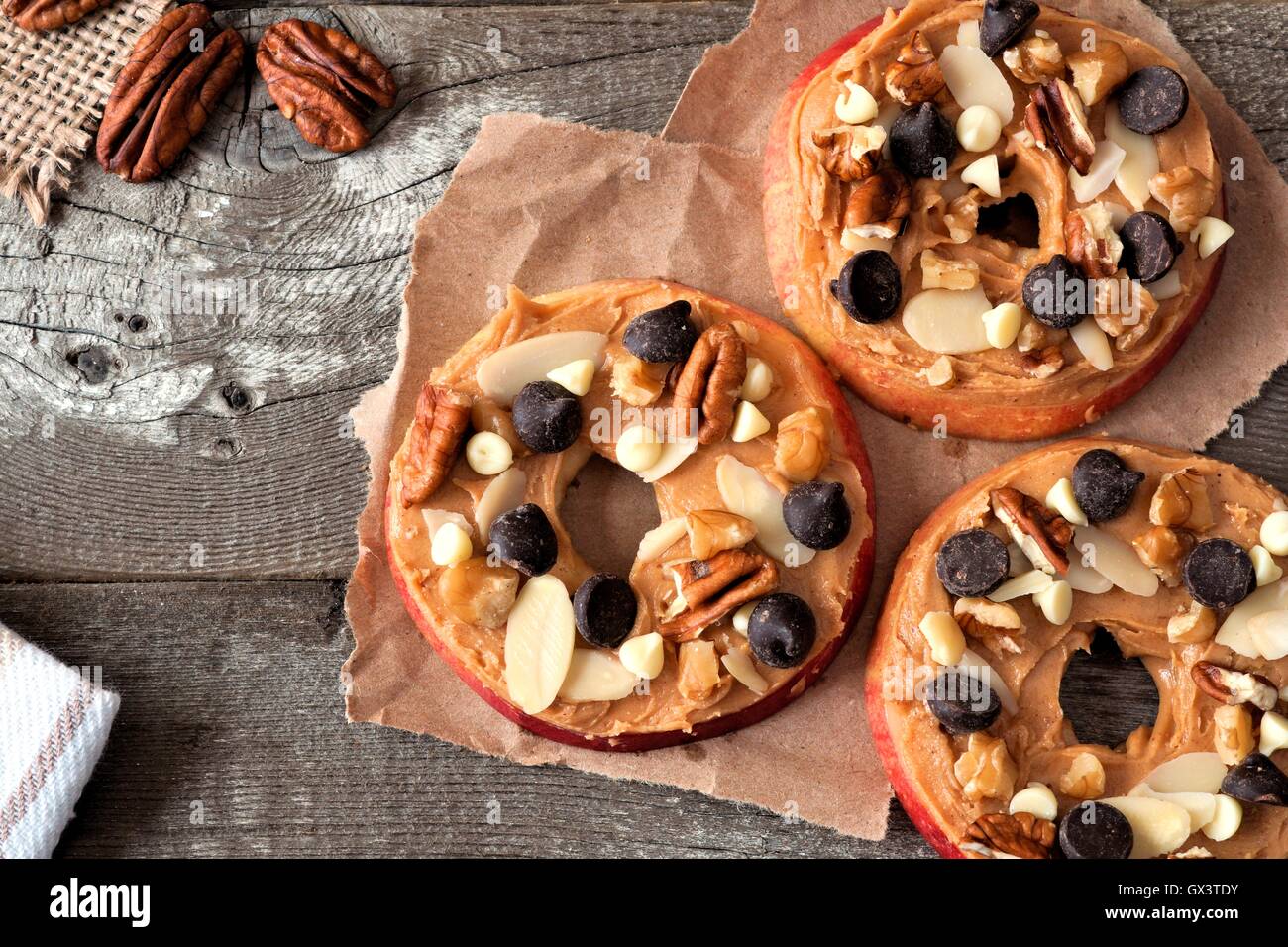 Apfel Runden mit Erdnussbutter, Schokolade-Chips und Nüssen, nach unten gerichtete Blick auf Papier mit rustikalen Holz Hintergrund Stockfoto