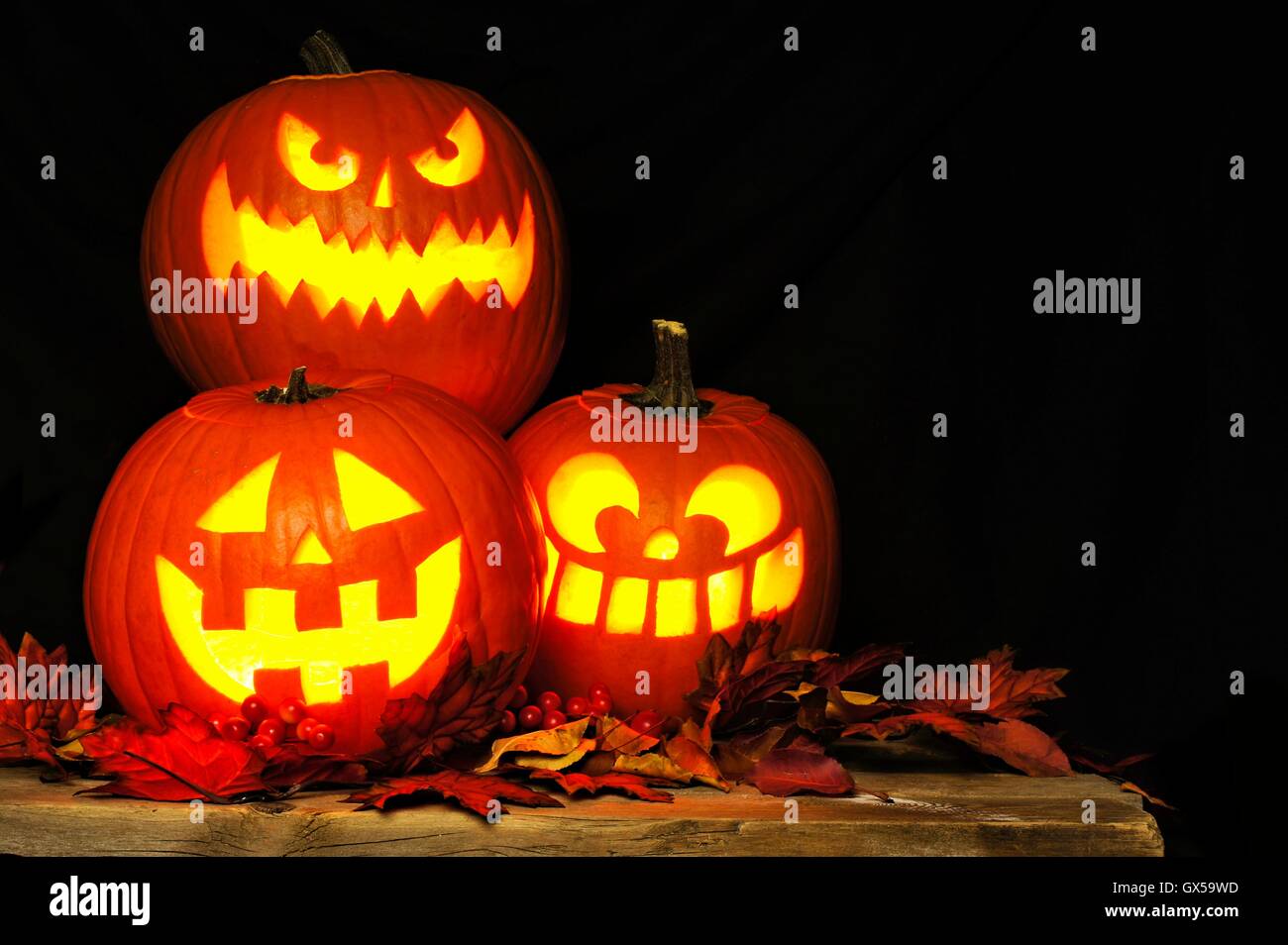Gestapelte Halloween Jack-o-Laternen beleuchtet in der Nacht mit altem Holz und Blätter im Herbst Stockfoto