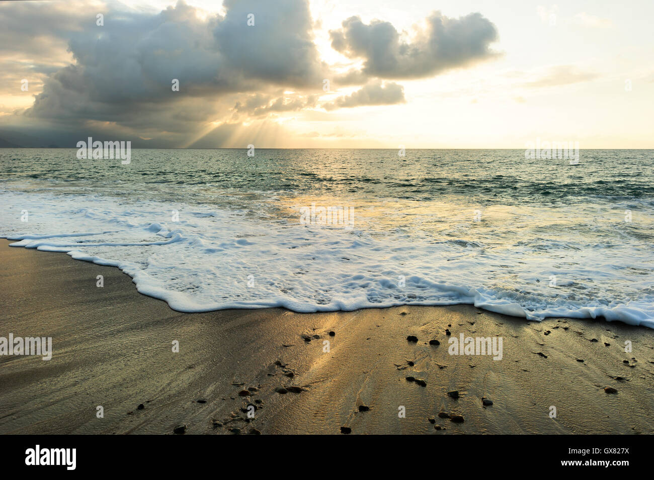 Sonnenuntergang Meer Strahlen ist eine helle erhebend Seenlandschaft mit Sonnenstrahlen durch die Wolken zu brechen, wie eine sanfte Welle ans Ufer Rollen. Stockfoto