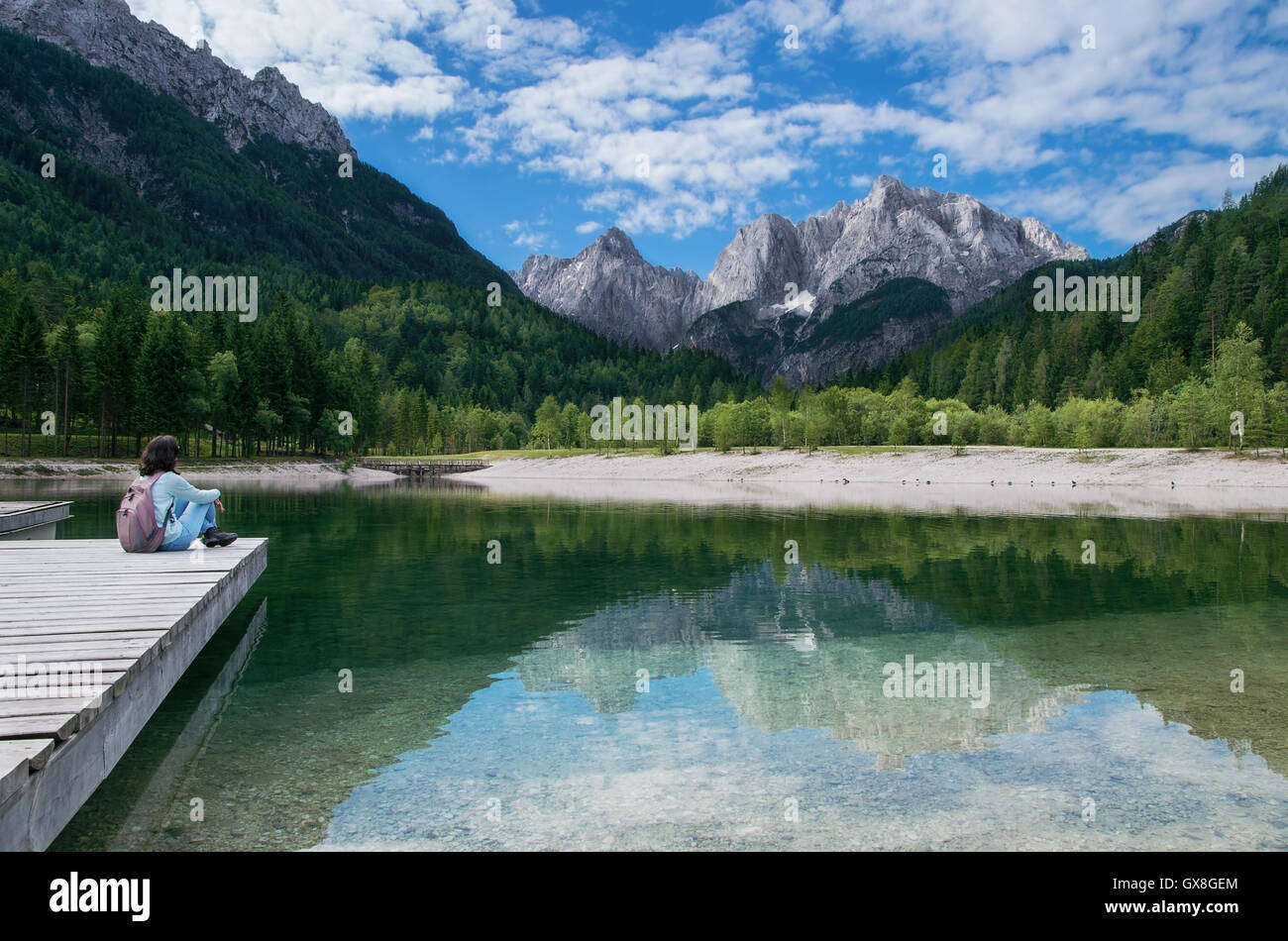 Blick auf die Julischen Alpen von Kranjska Gora mit Jasna-See und Mädchen sitzen am Pier in Slowenien Stockfoto