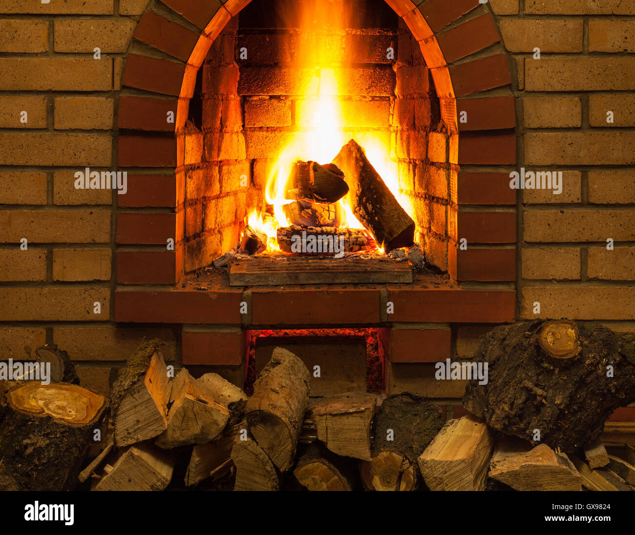 Haufen Brennholz und Zungen aus Feuer in indoor gemauerten Kamin im Landhaus Stockfoto
