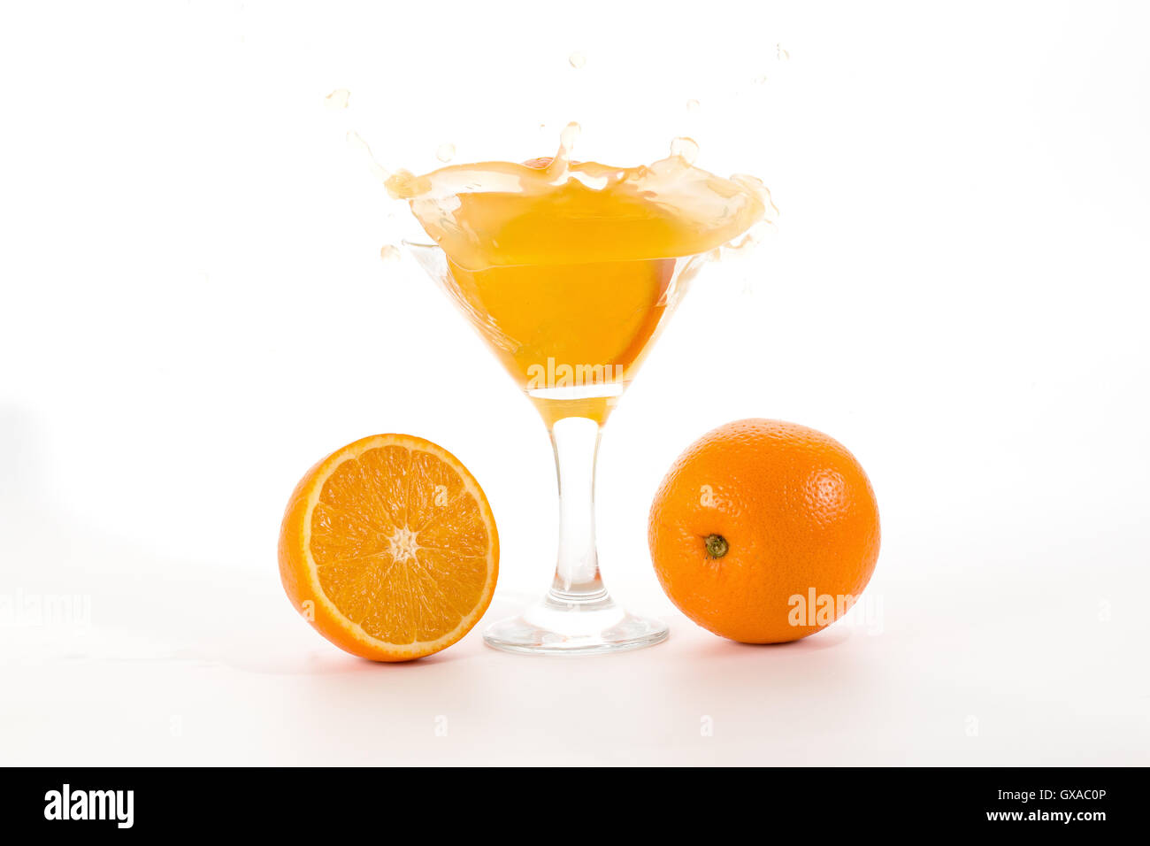 Orangenscheibe verliebt sich in ein Glas mit einem Cocktail und wirft eine Menge Spritzer auf weißem Hintergrund Stockfoto