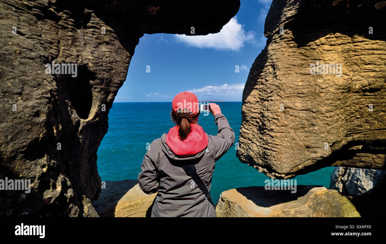 Portugal: Frau nehmen Momentaufnahme der Blick auf das Meer mit Smartphone durch ein Naturstein-Fenster Stockfoto