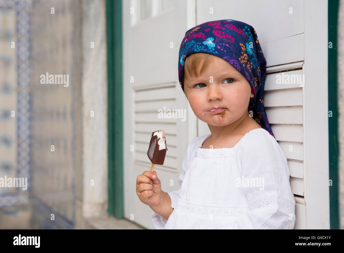 Porträt von weiblichen Kleinkind gelehnt Fensterläden essen Eis am Stiel, Beja, Portugal Stockfoto Porträt von weiblichen Kleinkind gelehnt Fensterläden essen Eis am Stiel, Beja, Portugal Stockfoto