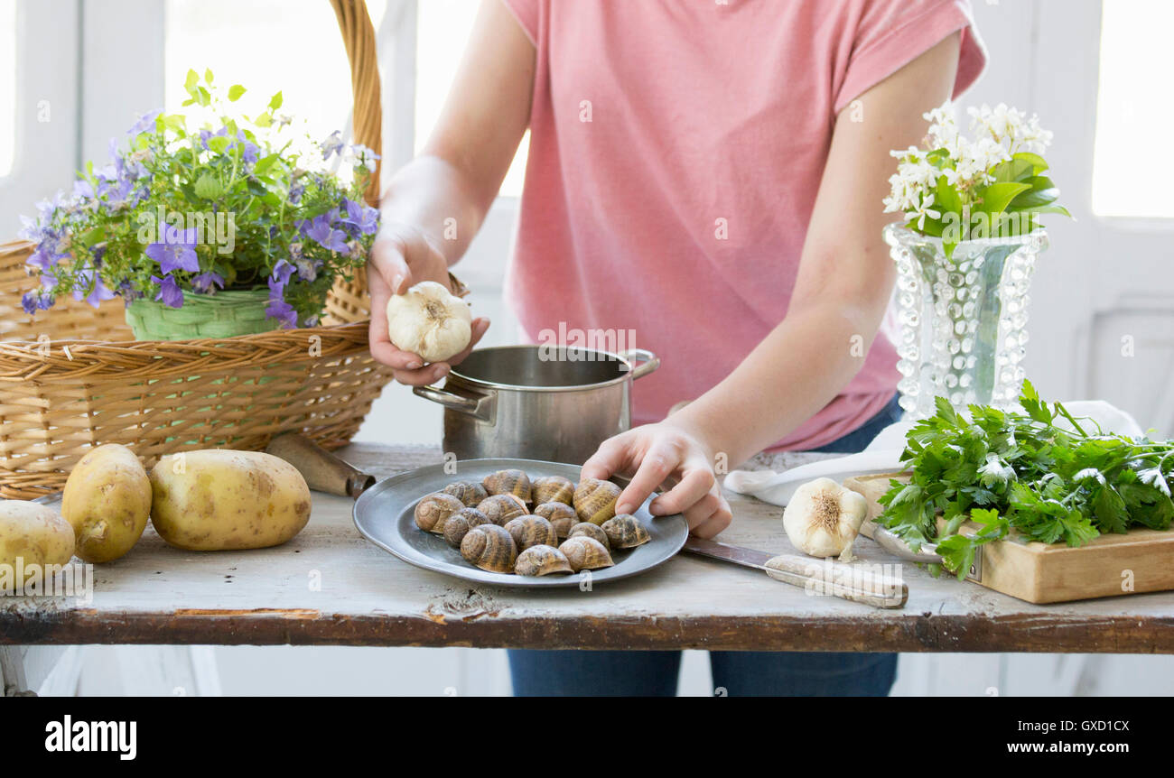 Junge Frau, die Vorbereitung von Schnecken und Knoblauch am Küchentisch, Vogogna, Verbania, Piemont, Italien Stockfoto