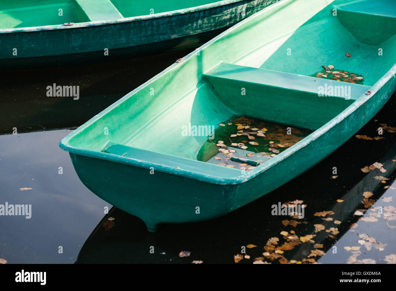 Zwei grüne Boote im Herbst See. Ende der warmen Jahreszeit. Eines der Boote ist voll von Regenwasser und abgestorbene Blätter. Stockfoto