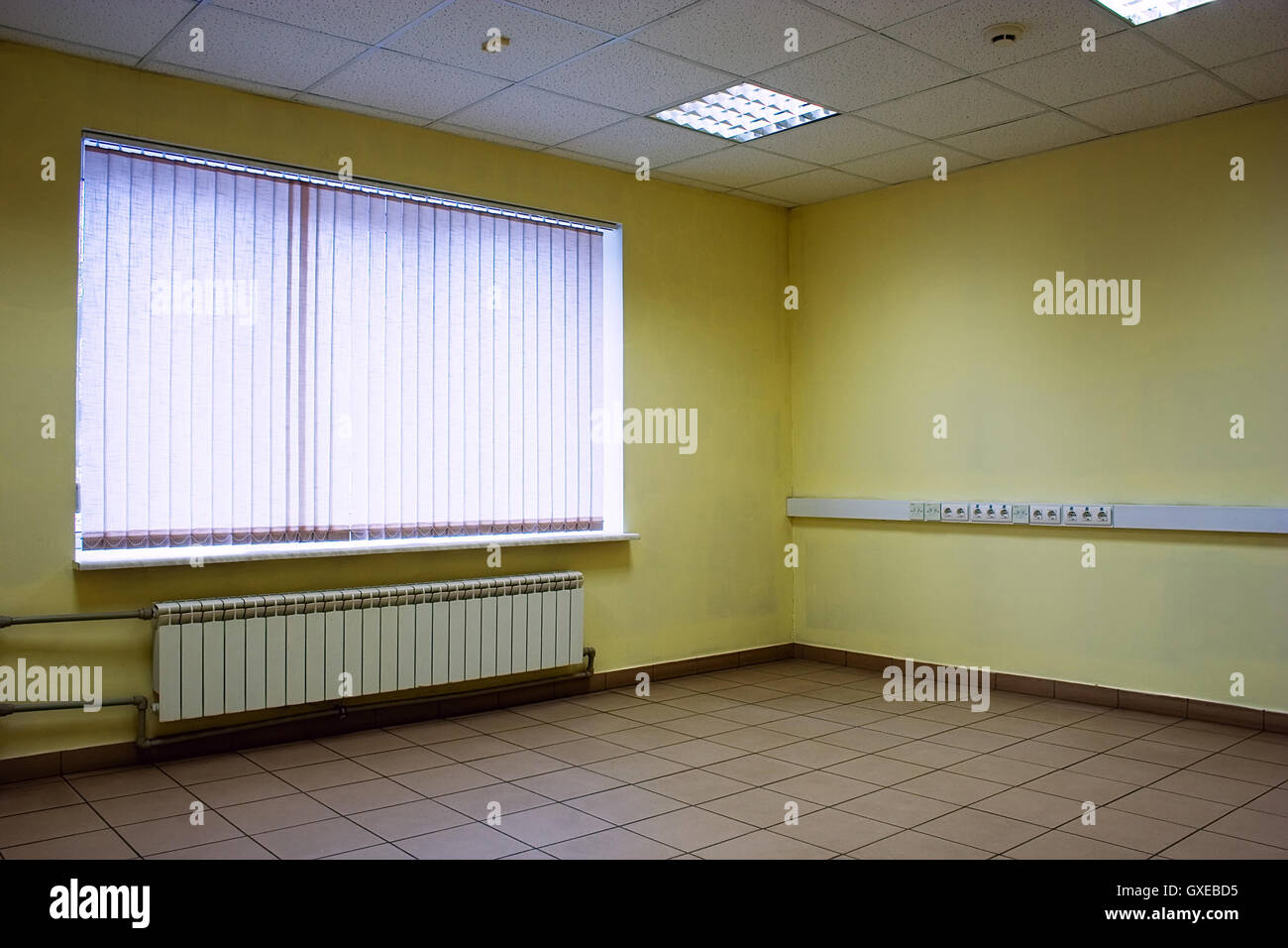 Ecke des leeren Büroraum mit Boden von Steinen, Decke, Lampen, gelbe Wände und Fenster mit Jalousie geschlossen Stockfoto