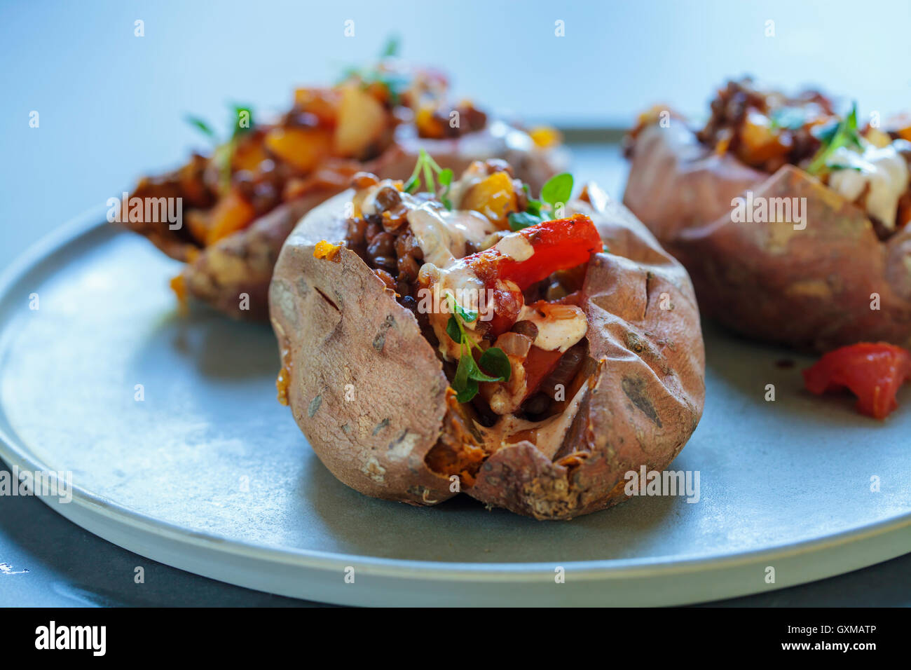 Süßkartoffeln mit würzigen Linsen, gelbe Paprika und Tomaten füllen, Chipotle saurer Sahne, Thymian und Knoblauch Blumen Stockfoto
