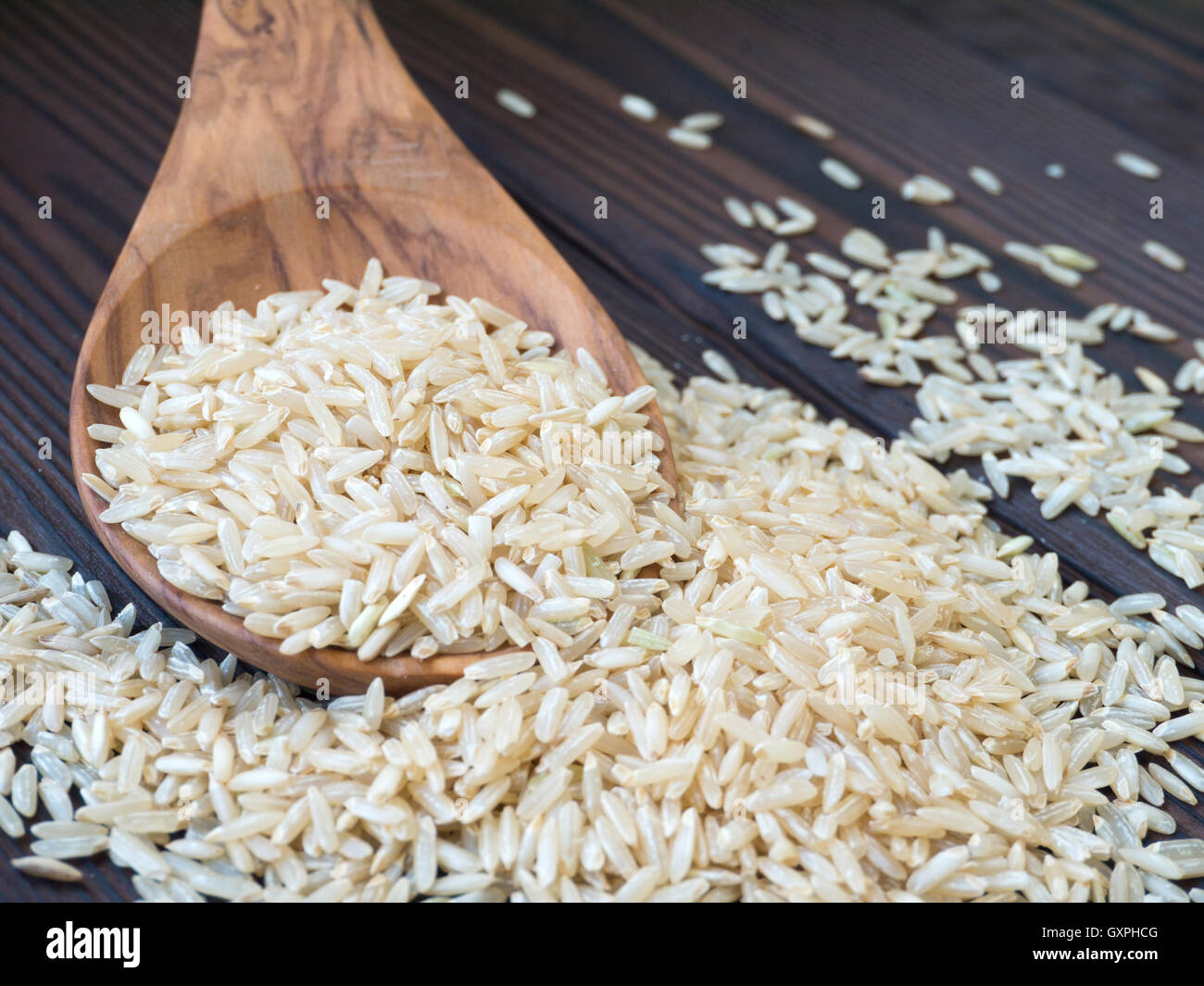 Brauner Reis in den Holzlöffel auf dunklem Holz strukturiert Planken Stockfoto