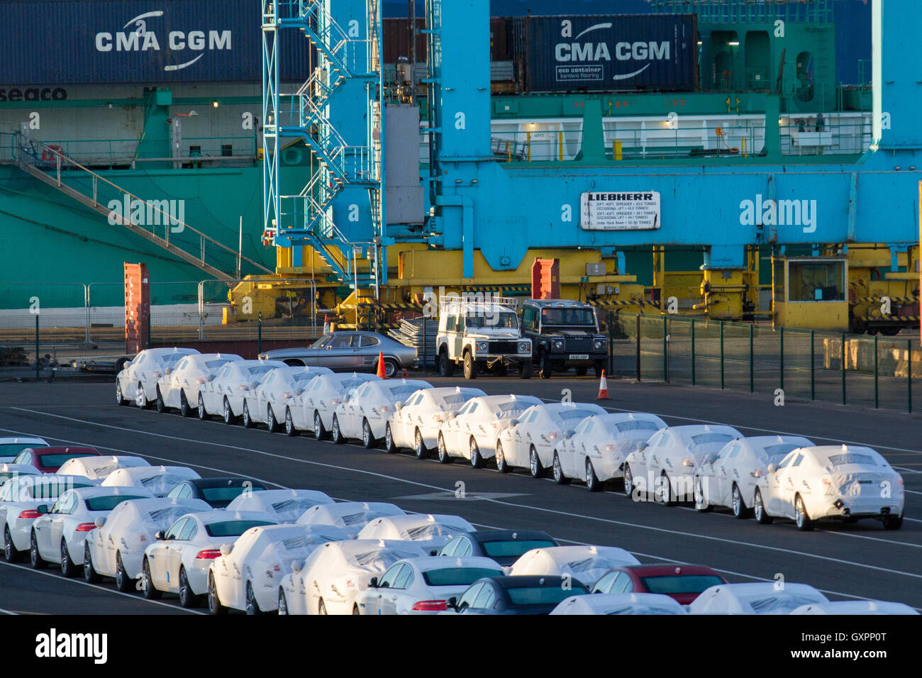 Autos, die auf das Verladen am Dock warten; New Luxury British fertigte Autos unter Wraps, verpackt zum Schutz für den Export aus dem Vereinigten Königreich an den Seaforth Docks. Weiß umhüllte, neue britische Jaguar & Land Rover Fahrzeuge für den Export, die am Kai von Liverpool für den Export stehen. CMA CGM Schiff am Peel Ports £300 m tiefen Wasser Container Terminal, das jetzt die größten Containerschiffe der Welt, Merseyside, Großbritannien, handhaben kann Stockfoto