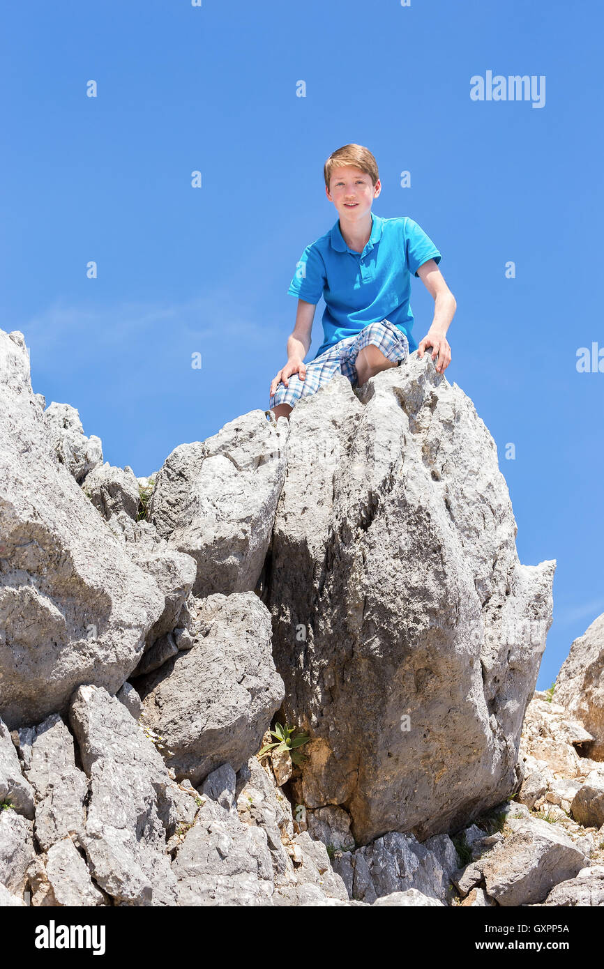 Kaukasische Teenager auf Felsen sitzend, mit blauem Himmel Stockfoto