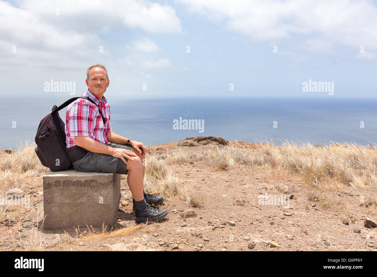Kaukasischen Mann mit Rucksack sitzt bergauf auf dem Meer Küste Stockfoto