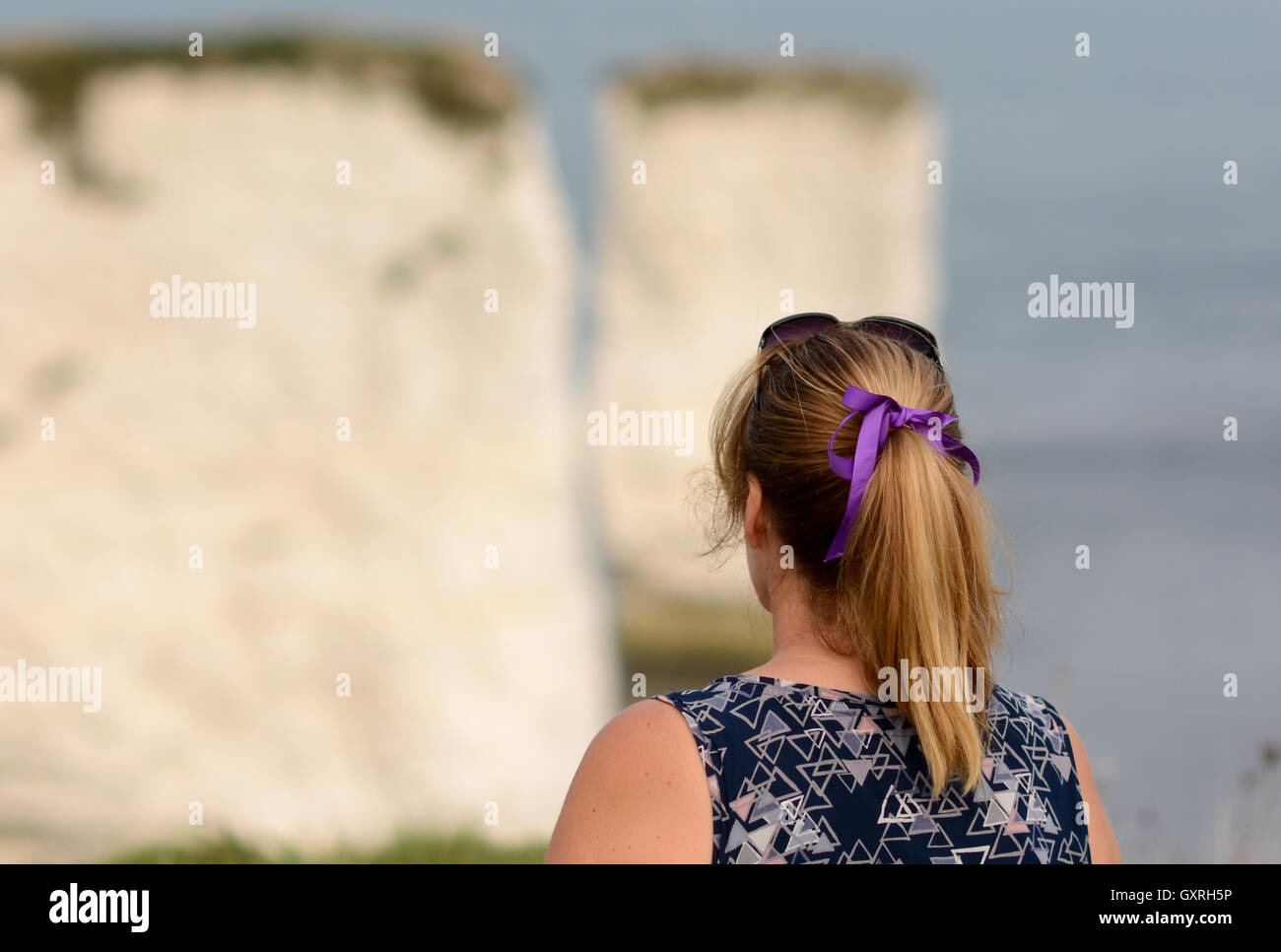 Frau auf der Suche heraus um zu sehen, über Felsen suchen nachdenklich mit einem lila Band und Pony Schweif. Stockfoto