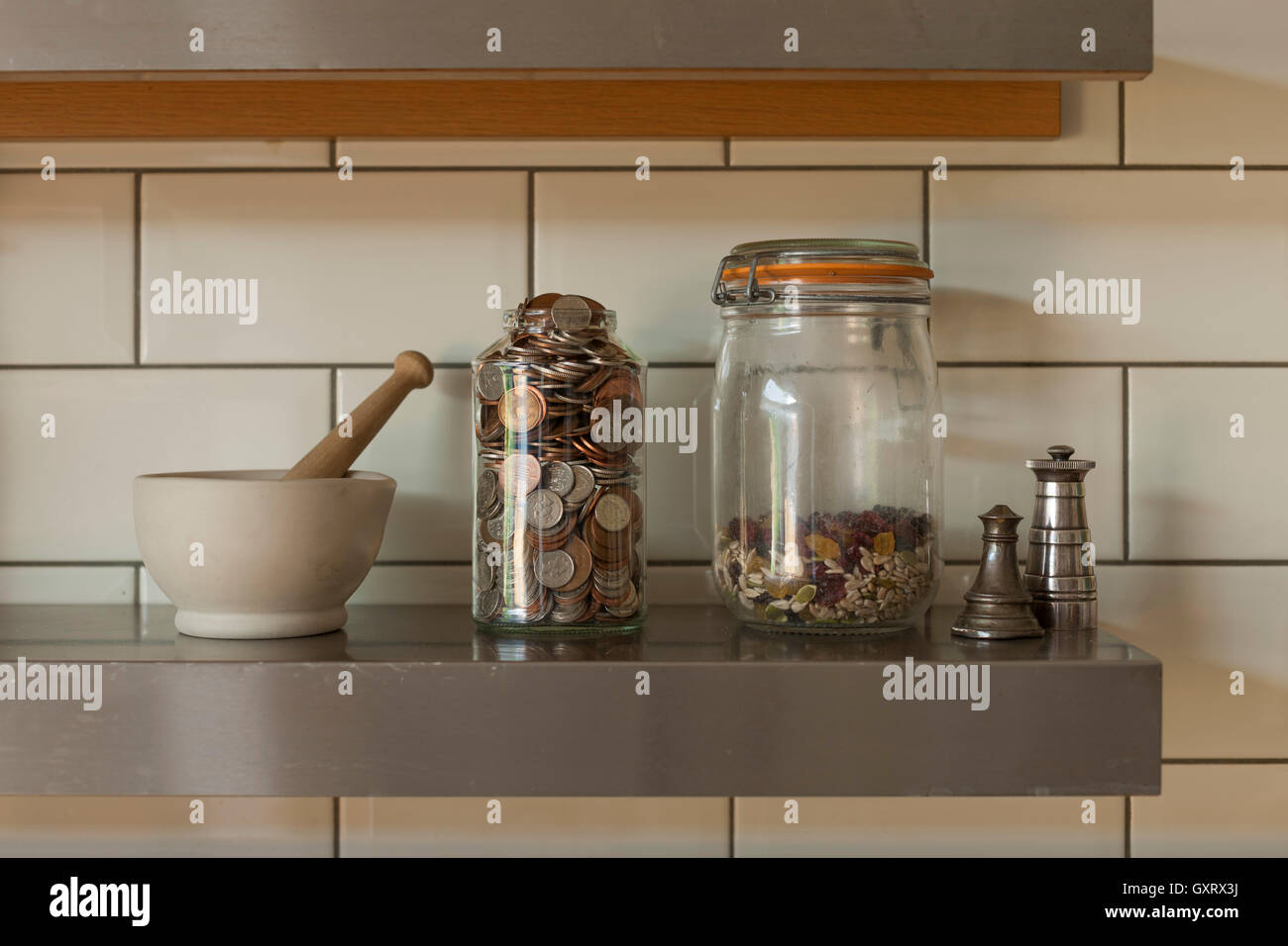 Glas mit Münzen, Zutaten und Stößel und Mörser auf Küchenregal Stockfoto
