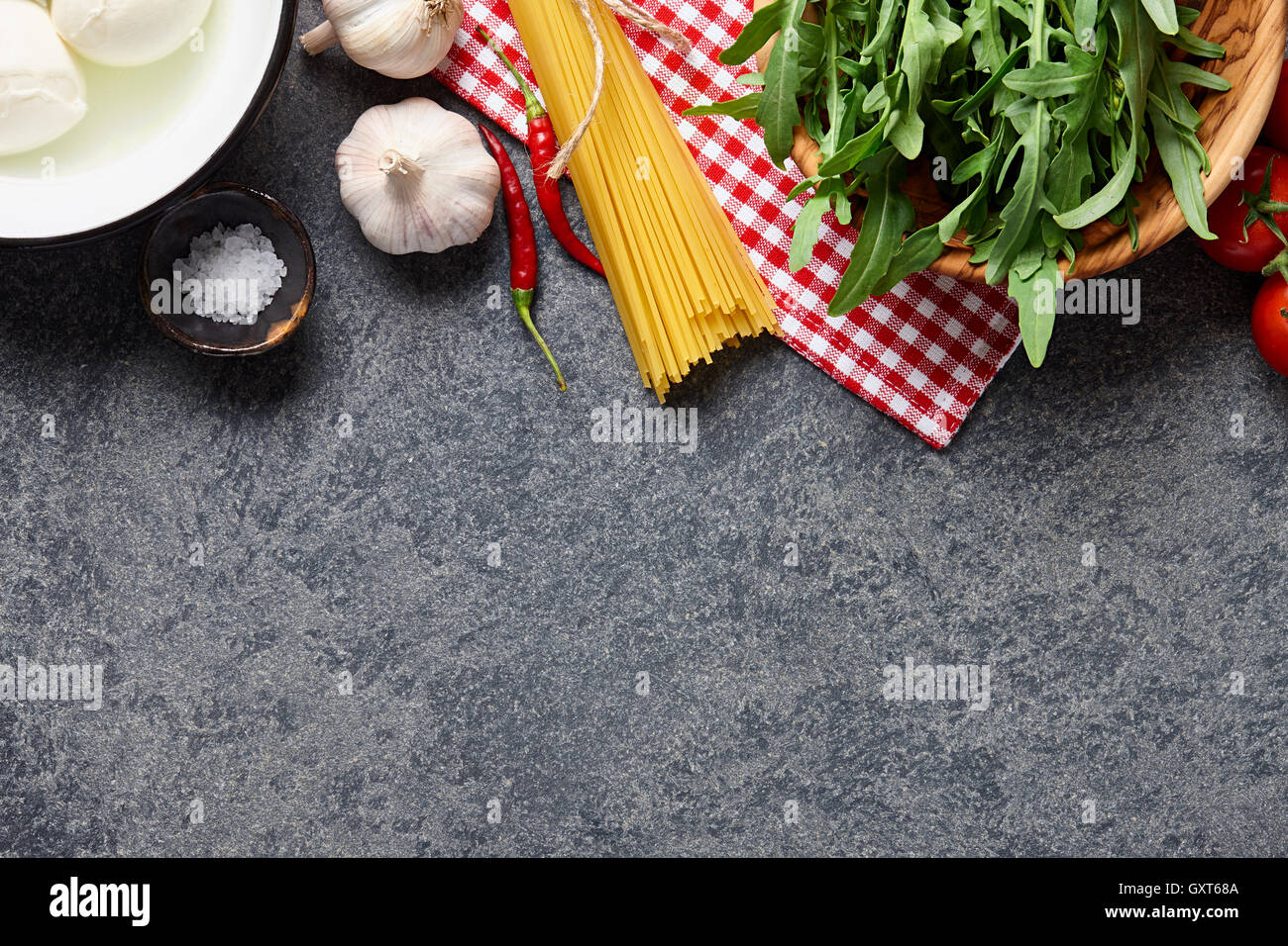 Italienische Küche Zutaten Hintergrund mit rohen Spaghetti, Rucola, Mozzarella-Käse, Paprika, Knoblauch, Salz und Tomaten Stockfoto