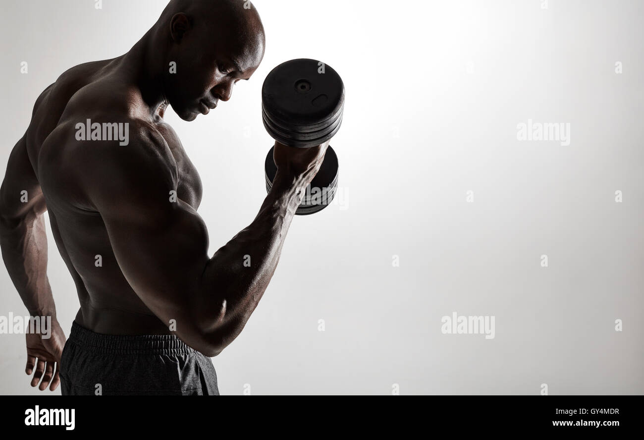 Schuss von gesunden muskulösen jungen Mann tun Gewicht trainieren mit Hanteln vor grauem Hintergrund. Bodybuilder tun schweres Gewicht Stockfoto