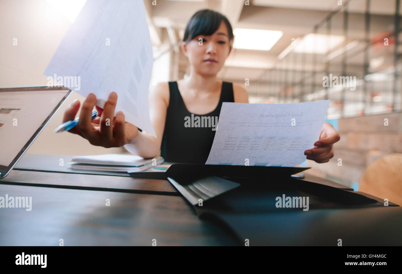 Schuss von Frau sitzt an ihrem Schreibtisch und Dokumente durchlaufen. Asiatische Geschäftsfrau mit Papierkram im Büro. Stockfoto
