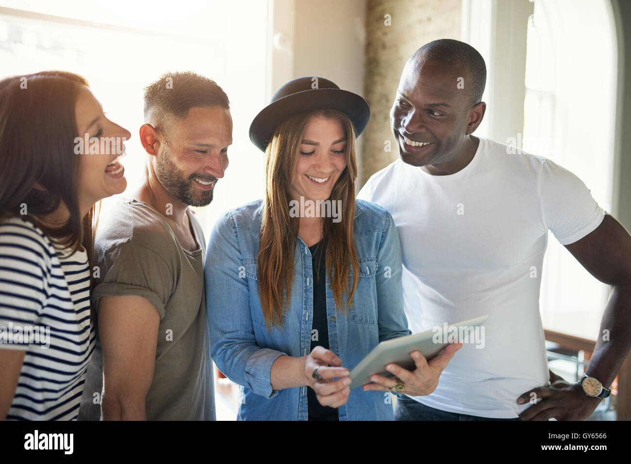 Männliche und weibliche Freunde Lächeln auf Tablet-Computer stehen zusammen mit großen Fenstern, wie Sonne in gießt Stockfoto