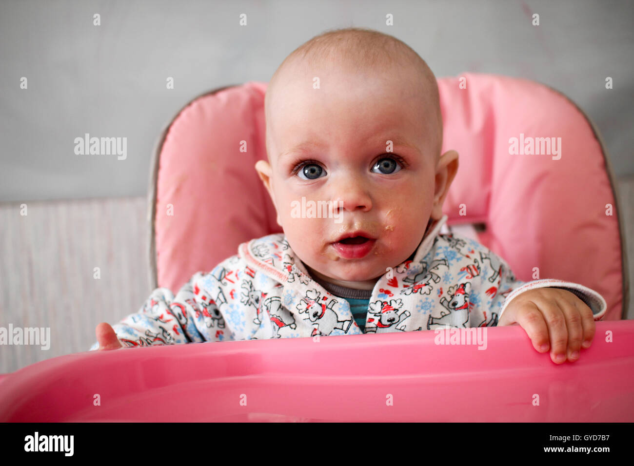 Schöne Baby isst Brei aus Mamas Hand. Er sitzt auf einem rosa Kinder "Stuhl. Stockfoto
