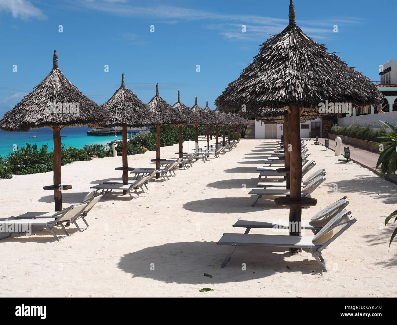 Blick entlang einer Reihe von strohgedeckten Sonnenschirme Schatten an einem weißen Sandstrand vor einem strahlend blauen Himmel Stockfoto