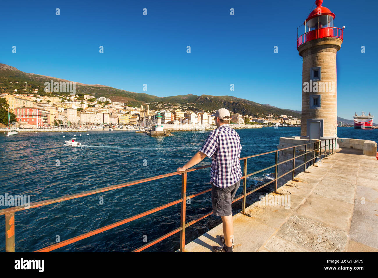 Junger attraktiver Mann, Blick auf die Altstadt der Stadt Bastia mit Joannis Babtistes Kathedrale, Leuchtturm und Boote, Corsica Stockfoto