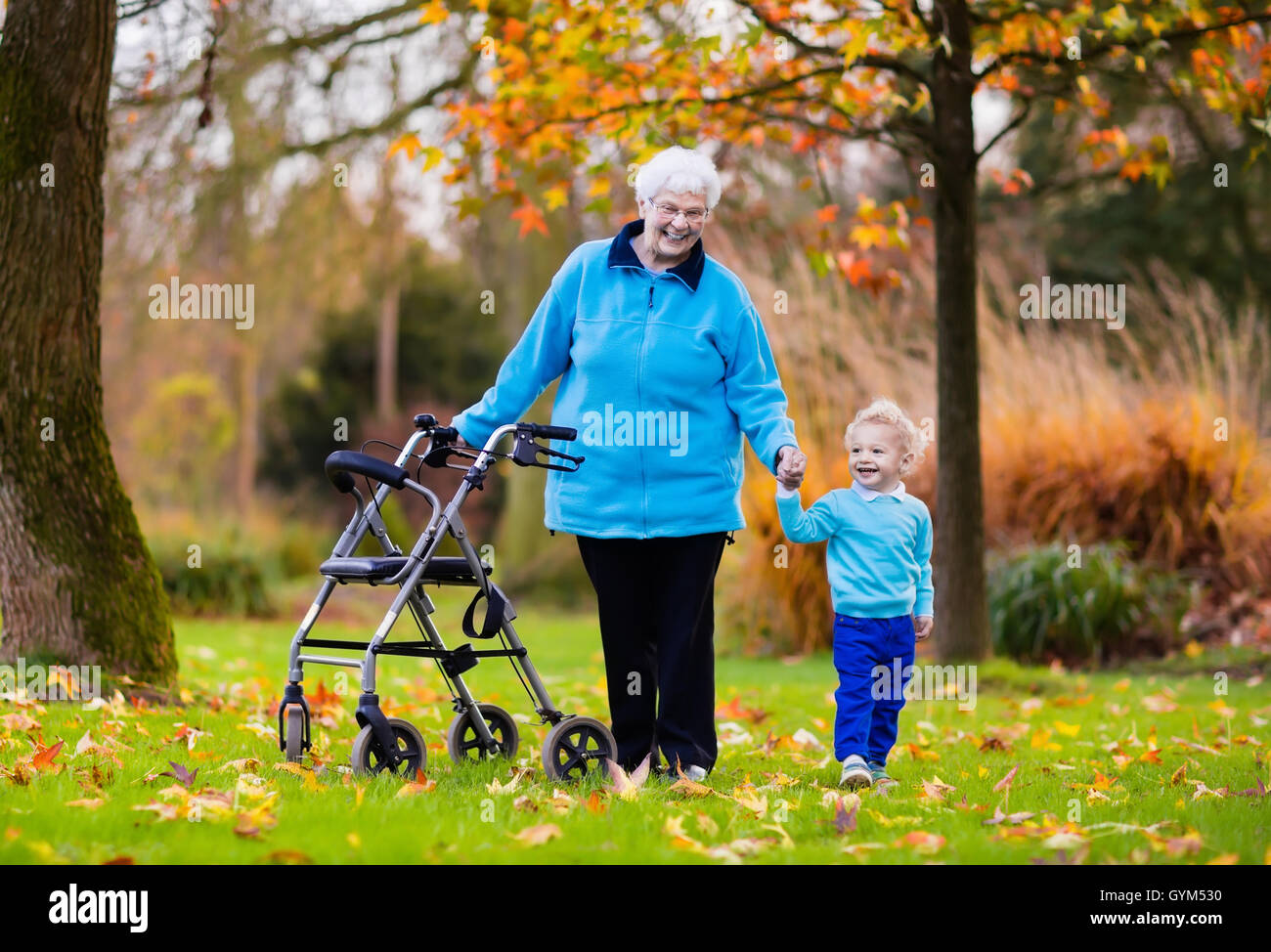 Glücklich senior Lady mit einer Gehhilfe oder Rollstuhl und Kinder. Großmutter und Kinder genießen Sie einen Spaziergang im Park. Stockfoto
