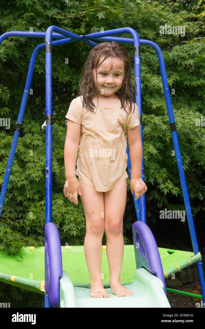 Niedliches aussehendes Mädchen, drei Jahre alt, stehen an der Spitze von einem Garten Rutsche Klettergerüst sehr nass, im Garten. Spielen. VEREINIGTES KÖNIGREICH. Juli Stockfoto