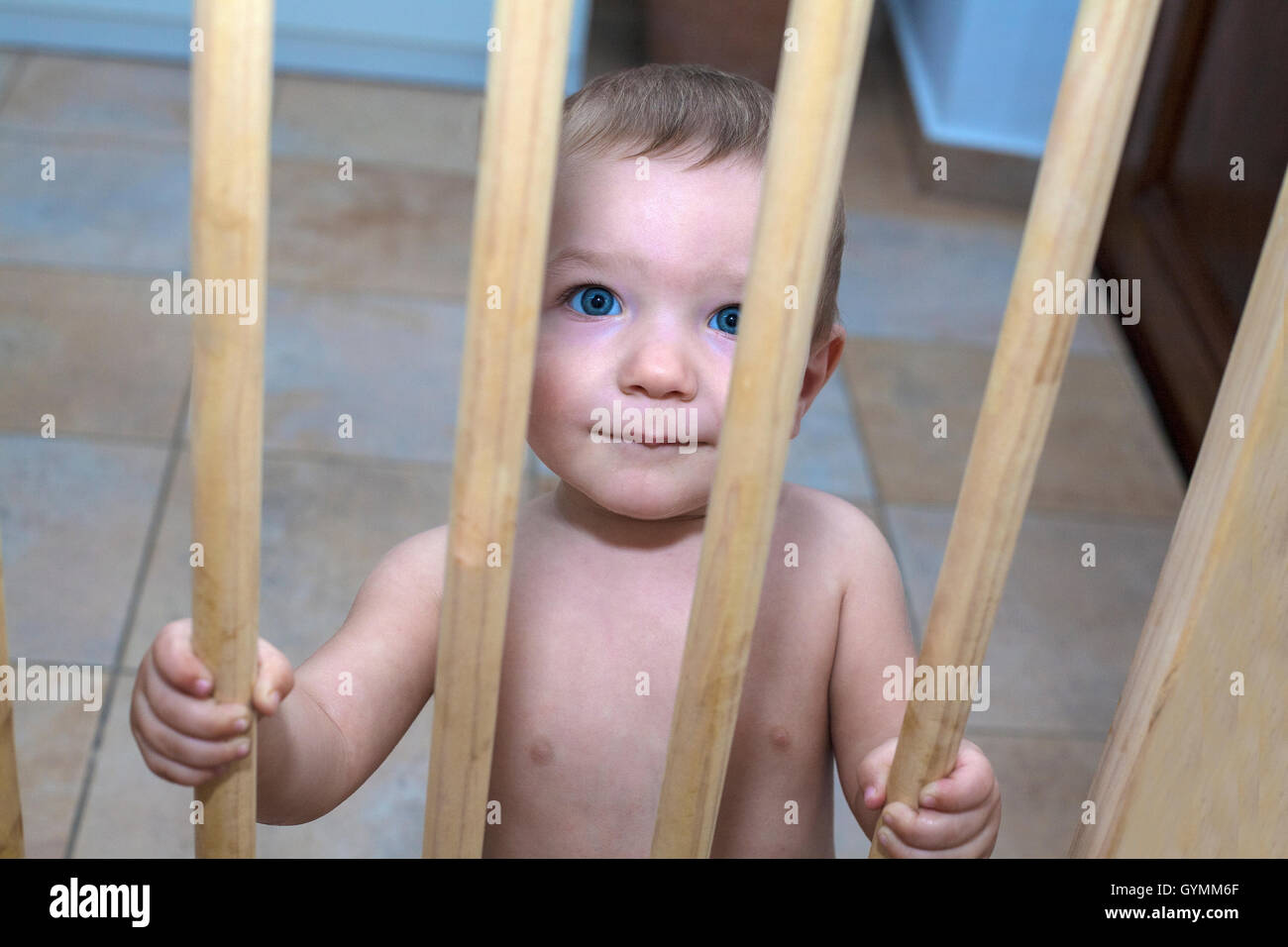 Einjährigen jungen hinter hölzernen Schutzgitter Treppe. Er versucht, nach oben gehen Stockfoto