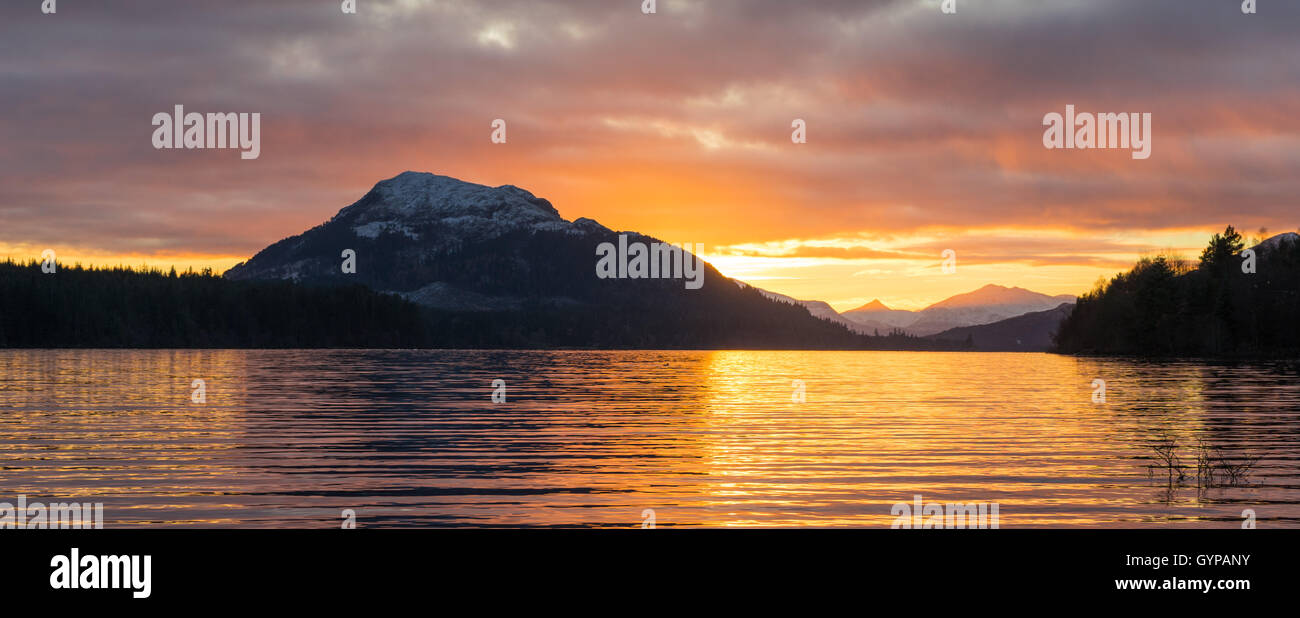 Sonnenuntergang mit Reflektion auf ruhigem Wasser mit Bergen im Hintergrund Stockfoto